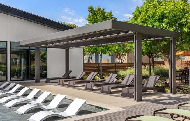 A row of sun loungers are arranged on a wooden deck next to a pool.