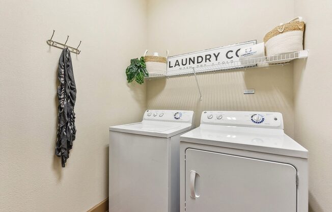 a washer and dryer in a laundry room with a shelf on the wall at Lakeline East Apartments, Cedar Park, TX