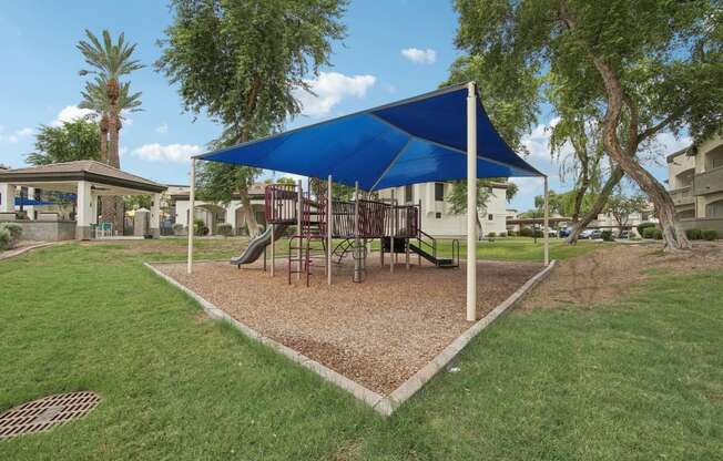 a playground with a swing set and a blue umbrella