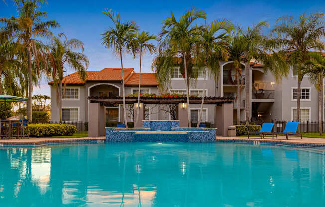 A large swimming pool in front of a house with a patio and palm trees.