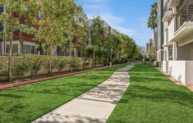 a walkway between two apartment buildings with green grass and trees
