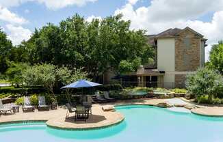 A pool with a blue umbrella and chairs in front of a house.