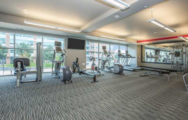 a gym with weights and cardio equipment on the floor and large windows