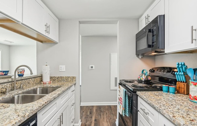 a kitchen with white cabinets and granite counter tops and a black microwave