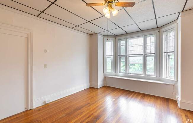 A room with a ceiling fan and a window with a view of trees.