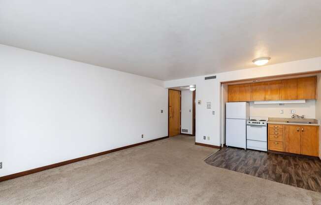 the living room and kitchen of an apartment with white walls and wood floors