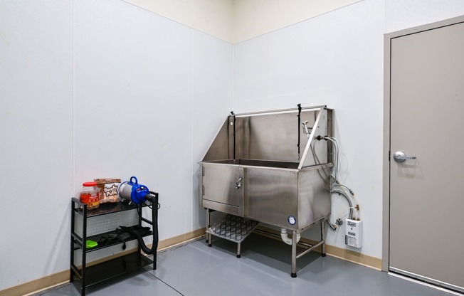 a stainless steel tub in a white room with a black cart next to it