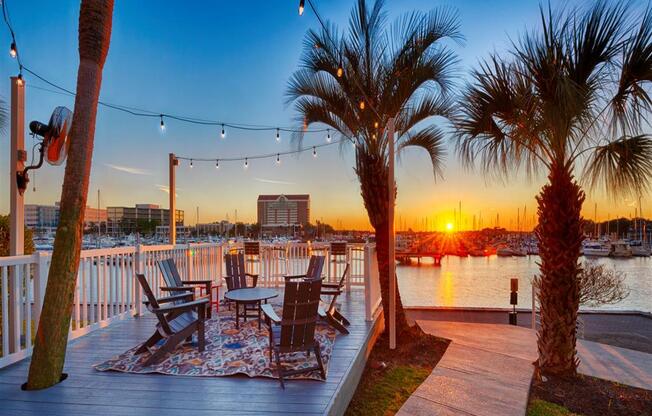 a deck with chairs and palm trees overlooking the water at sunset