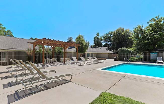 A pool area with sun loungers and a pergola.