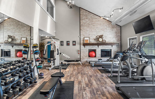 a gym with weights and cardio equipment and a television