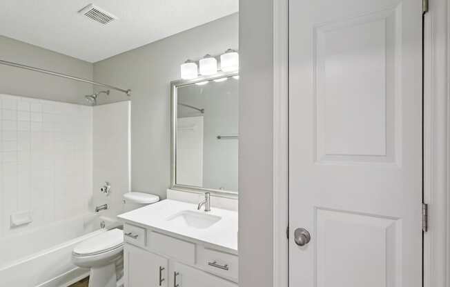A white bathroom with a toilet, sink, and mirror.