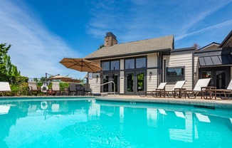 A large swimming pool in front of a house with a sun lounger.