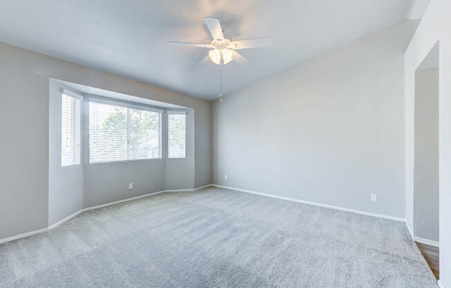 an empty living room with a ceiling fan and a window