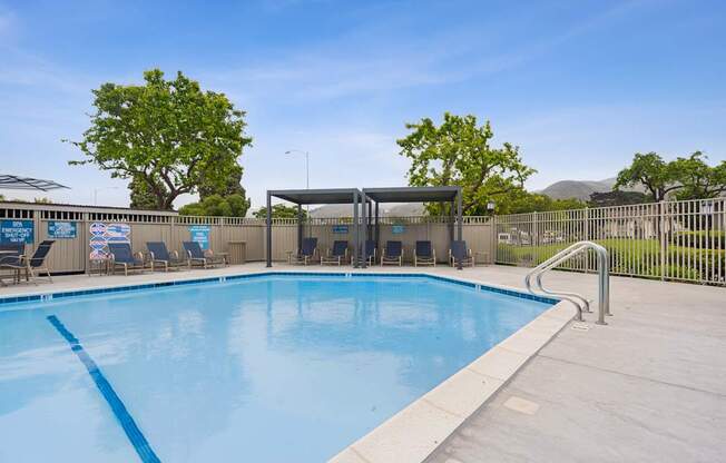 A large outdoor swimming pool with a blue tiled edge and a metal fence surrounding it.