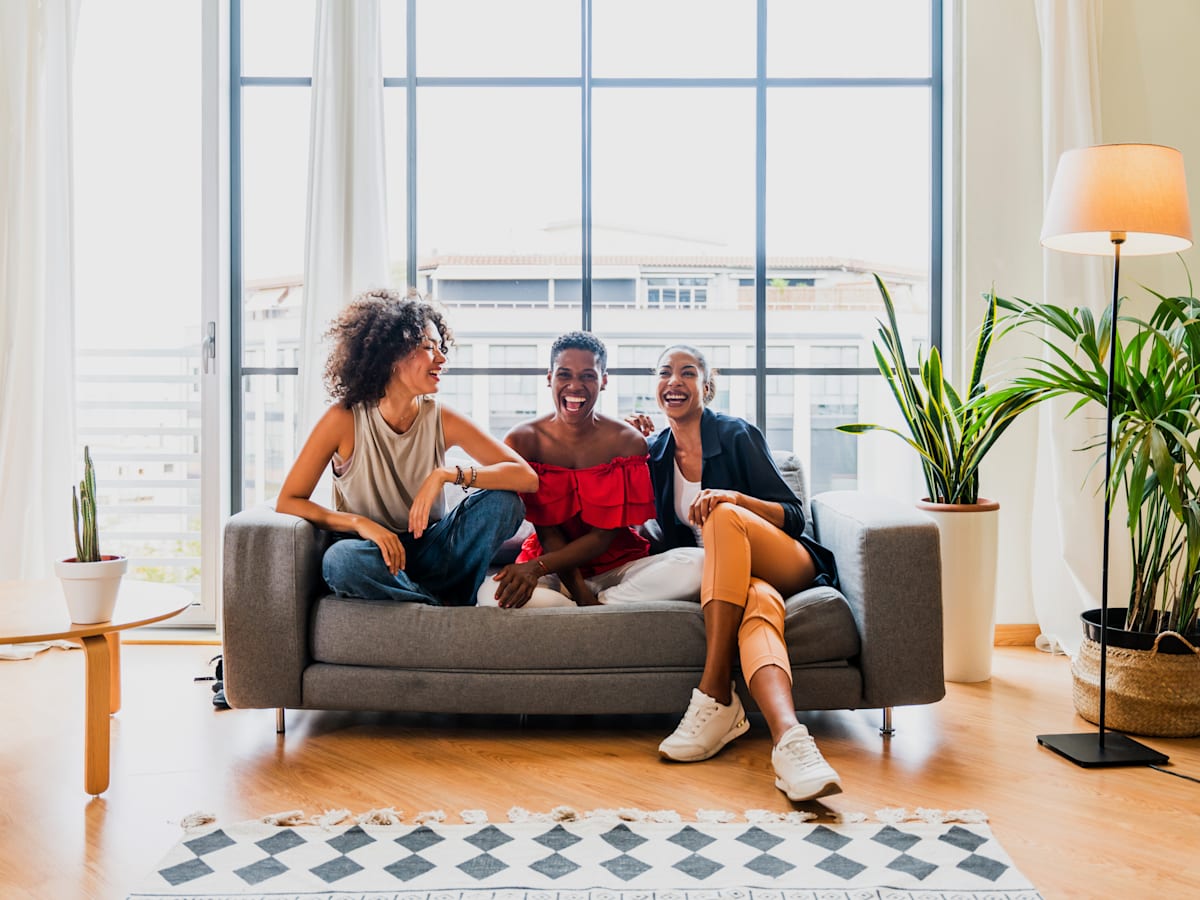 Three people are sitting on a couch in a bright room with large windows at Portofino Vineyards Apartment, Fort Myers, Florida