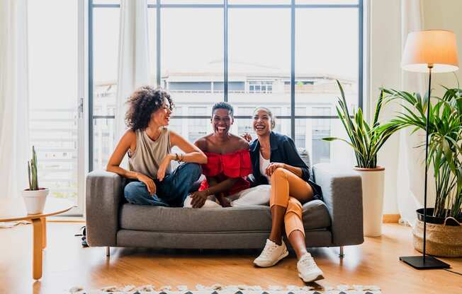 Three people are sitting on a couch in a bright room with large windows at Portofino Vineyards Apartment, Fort Myers, Florida