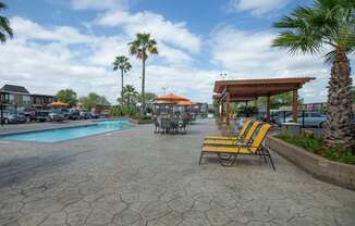 A pool area with a patio, chairs and umbrellas at Willow Creek Apartments, Texas