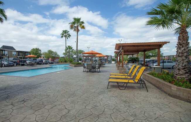 A pool area with a patio, chairs and umbrellas at Willow Creek Apartments, Texas