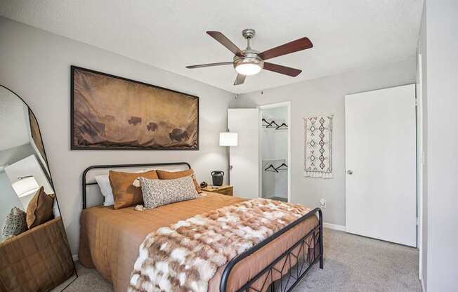 A bedroom with a bed, a ceiling fan, and a painting on the wall.