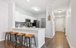 A kitchen with white cabinets and a white island with three stools.