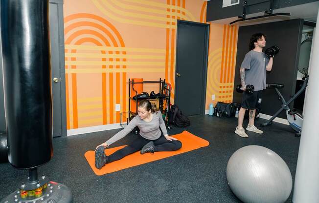 A man and a woman are exercising in a gym with orange and black accents.