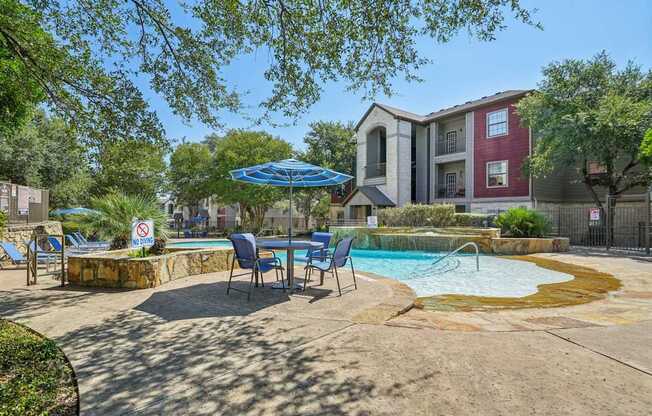 A pool area with a blue umbrella and chairs.