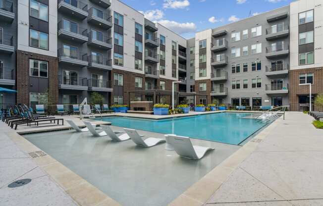 an apartment pool with chairs in front of an apartment building