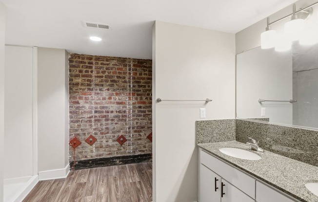 A bathroom with a brick wall and wooden floors.