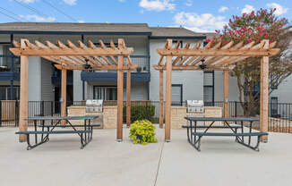a picnic area with two picnic tables and a barbecue grill in front of a building