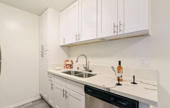 Kitchen with stainless steel dishwasher, double kitchen sink, wood style floors, light marble counter tops, white cabinets