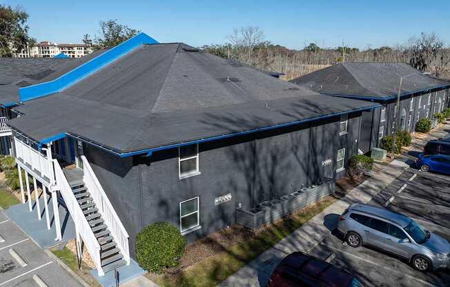 A grya building with a blue roof is surrounded by a parking lot at Mandarin Bay Apartments on San Jose Blvd