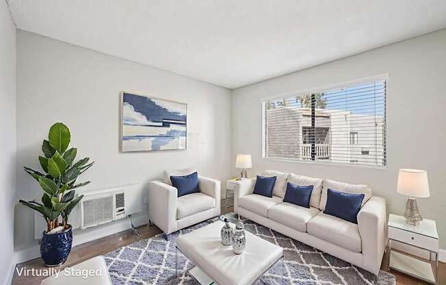 A living room with a white couch, a blue plant, and a painting on the wall.