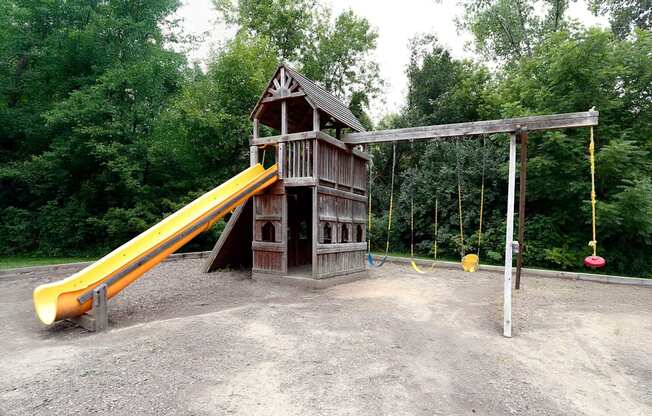 A playground with a yellow slide and a wooden swing set.