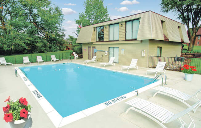 A pool with chairs and a house in the background.