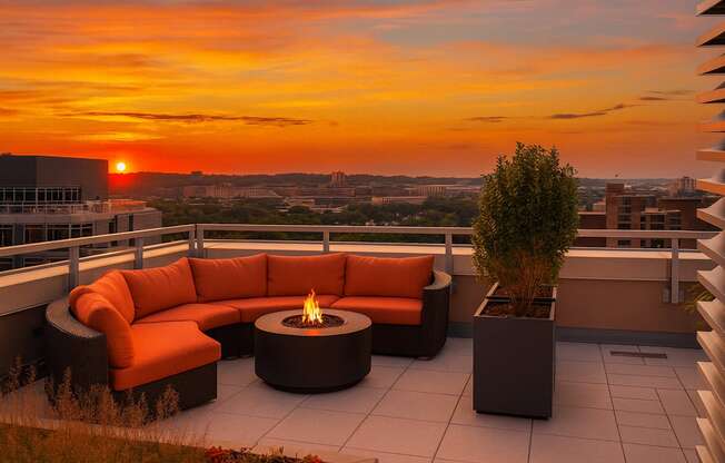 A patio with a fire pit and seating area overlooking a cityscape at sunset.