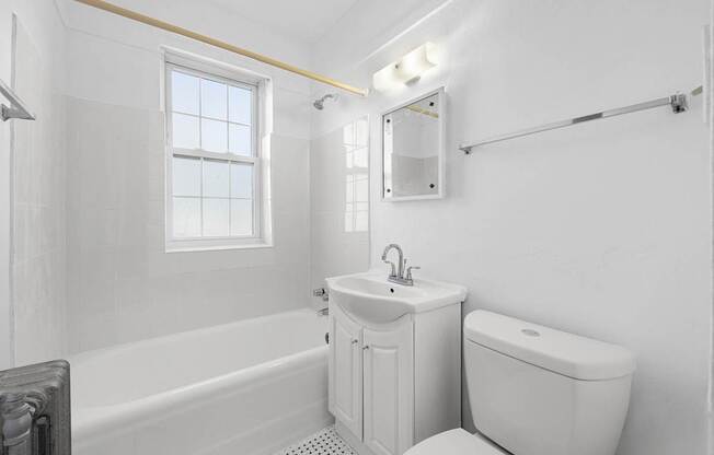 A white bathroom with a tub, toilet, sink, and mirror at Pleasant Oak Apartments, Oak Park, IL, 60302
