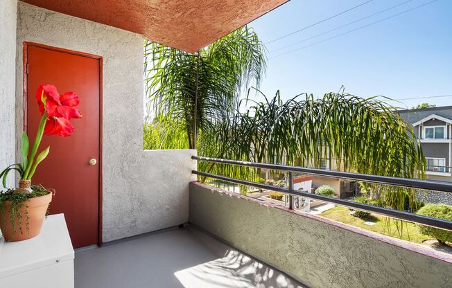a small balcony with a red door and a red flower in a pot
