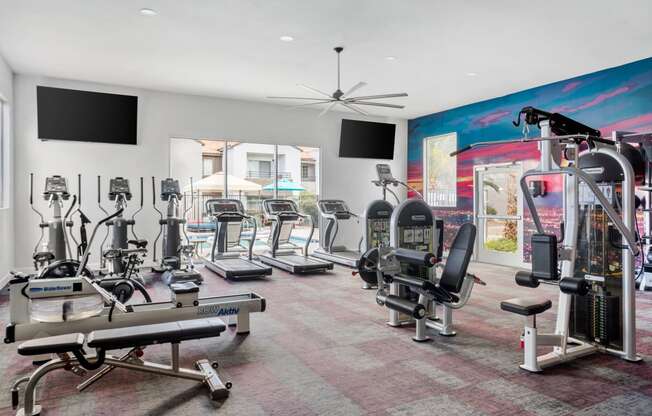 a spacious fitness room with cardio equipment and flat screen televisions