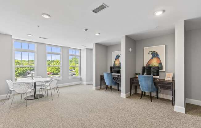 a living room with a table and chairs and a desk and windows