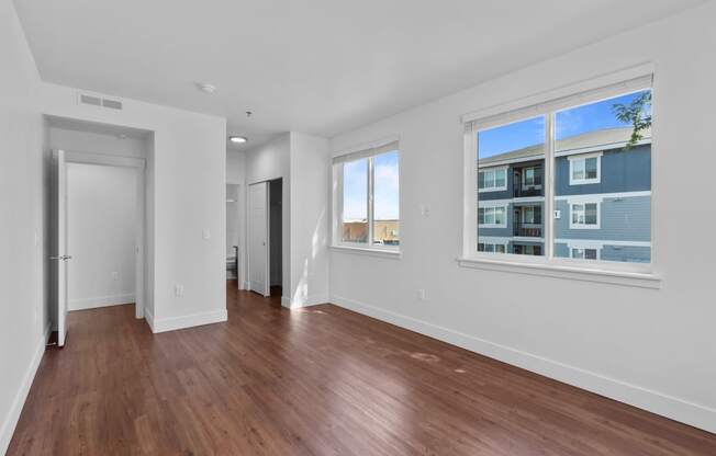 a bedroom with hardwood floors and three large windows