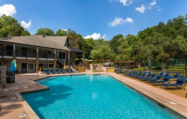 a swimming pool with blue lounge chairs around it in front of a house