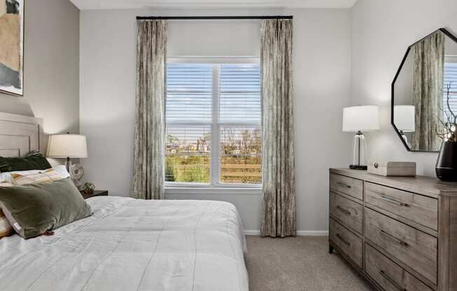 A well-lit bedroom with a large bed and a dresser with a mirror.