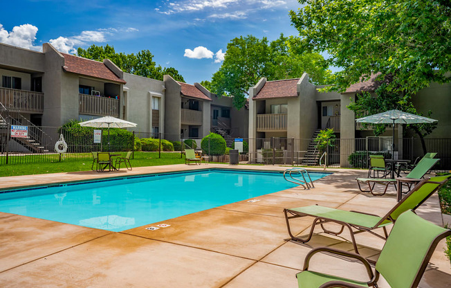 A swimming pool surrounded by chairs and umbrellas in front of apartment buildings.