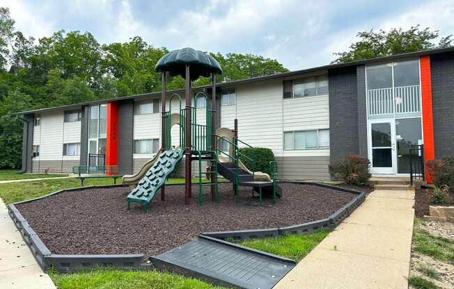 a playground with a slide and chairs in front of a building