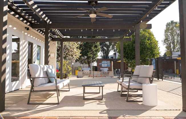 A patio with a white couch, two chairs, and a table under a pergola.