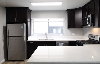 A kitchen with black and white counters and a stainless steel refrigerator