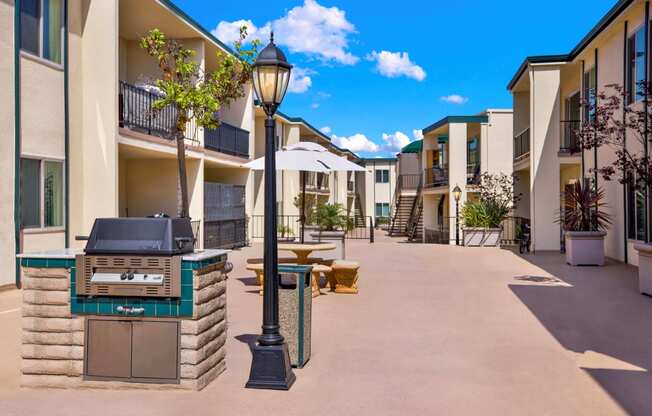 an outdoor patio with a grill and tables and apartments in the background at Casa Del Amo Apartments, Torrance, CA