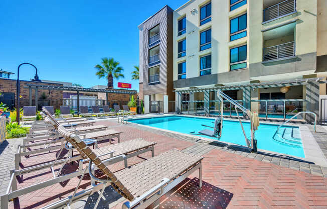 A pool area with sun loungers and a building in the background.