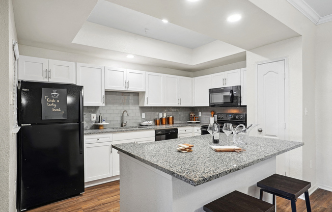 a kitchen with a granite counter top and a black refrigerator at La Ventura Apartments, Plano, Texas