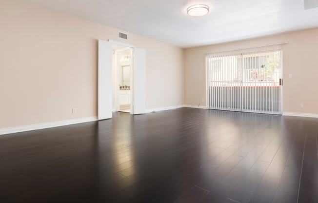 an empty living room with wood flooring and a door to a balcony